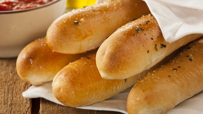 A group of cooked breadsticks topped with herbs sit in a white napkin