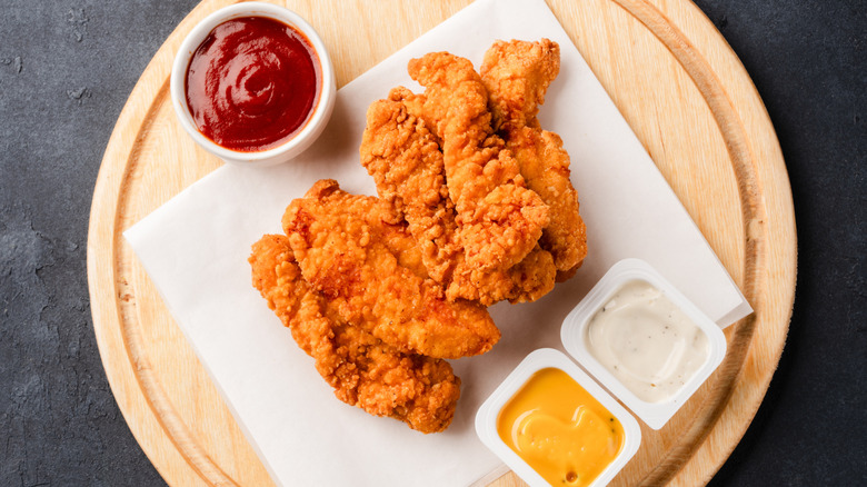 Chicken tenders on a wooden board with dipping sauces