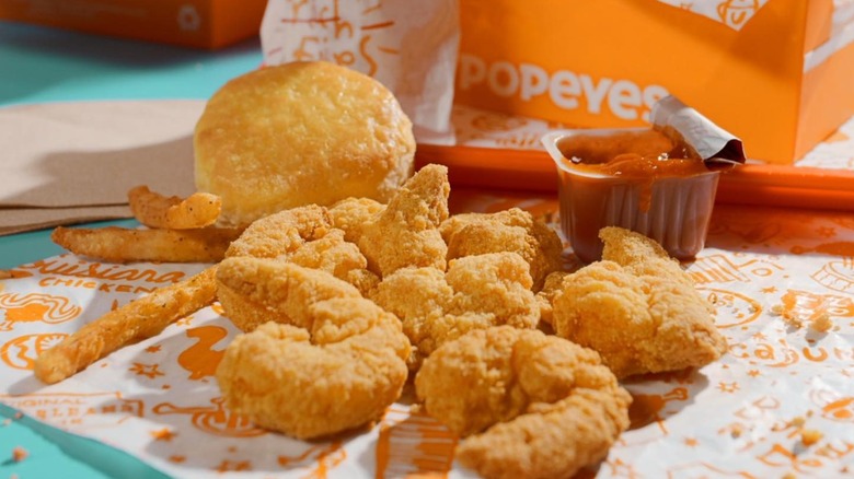 A platter of Popeyes food, including chicken, fries, and a biscuit, a biscuit, as well as a sauce container