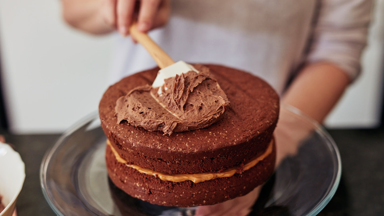 Baker spreading chocolate frosting on a chocolate cake