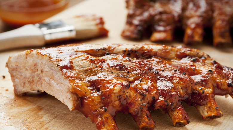 Rack of barbecued ribs on cutting board with barbecue sauce and brush