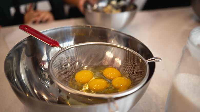raw eggs in sieve over mixing bowl