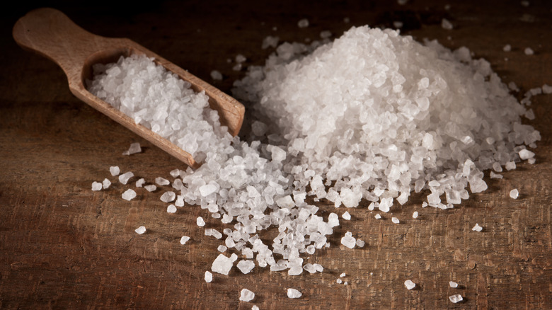 coarse salt in wooden scooper and a large pile against wood backdrop