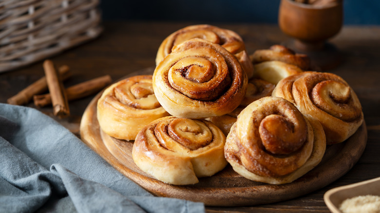 Fresh baked cinnamon rolls on a wooden board with cinnamon sticks, sugar and napkin Wooden and dark background