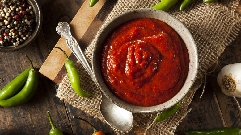 Sriracha sauce in a bowl with spoon and chili peppers