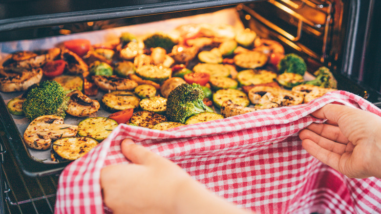 A person removes roasted vegetables from the oven on a sheet pan