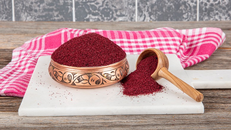 Ground red sumac spice powder in an etched metal bowl on kitchen cutting board