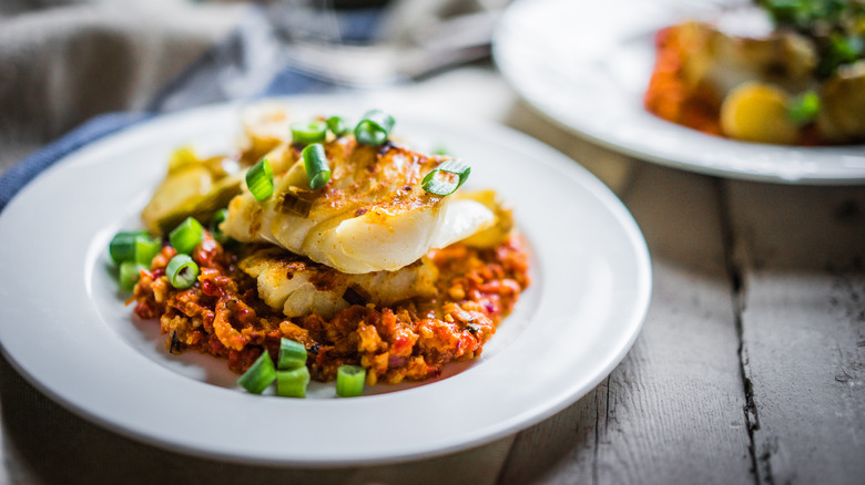 Roasted white fish with romesco sauce in a white dish on a wooden table