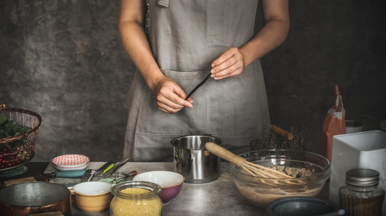 A cook in front of a baking station holding a vanilla pod