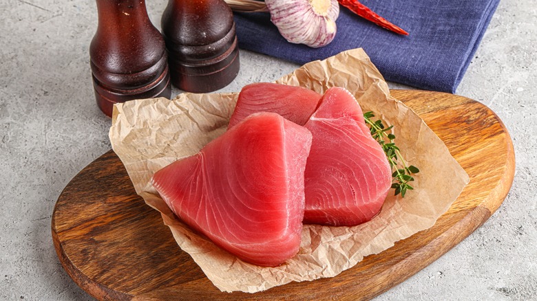 A pair of tuna fillets on parchment paper next to salt and pepper