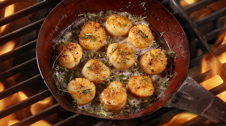 Scallops with butter and herbs in pan on grill