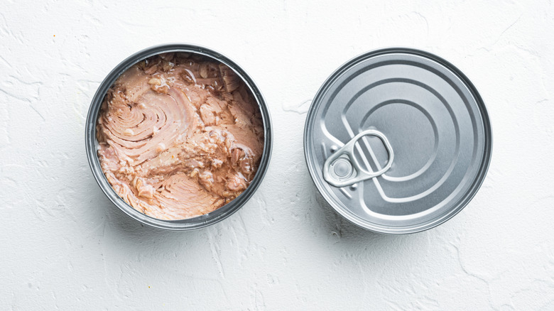 open and sealed cans of tuna on white background
