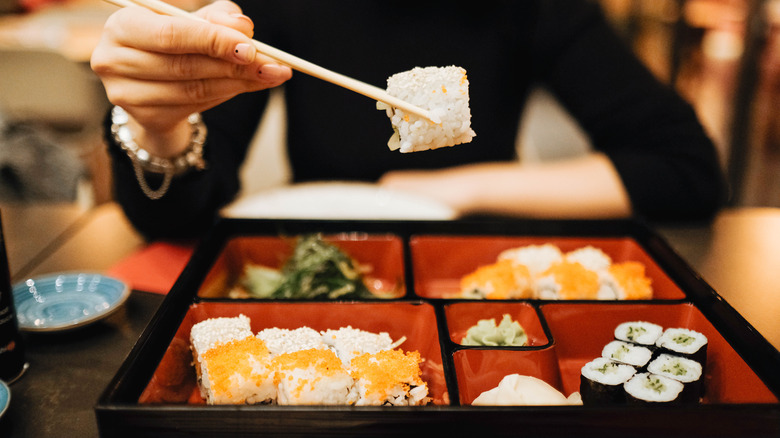 woman holding a piece of sushi with chopsticks