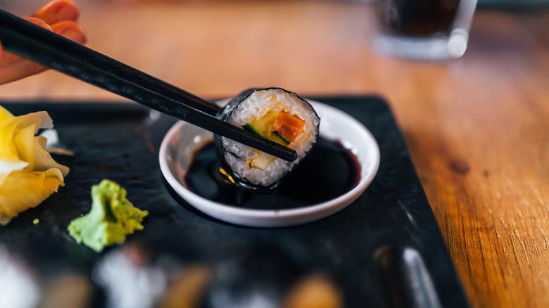 piece of sushi being dipped into soy sauce