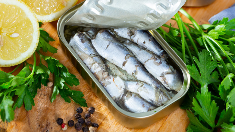 Sardines in a tin are surrounded by fresh parsley and lemons