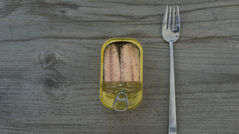 A half-opened tin of mackerel sits on a wooden surface with a fork next to it