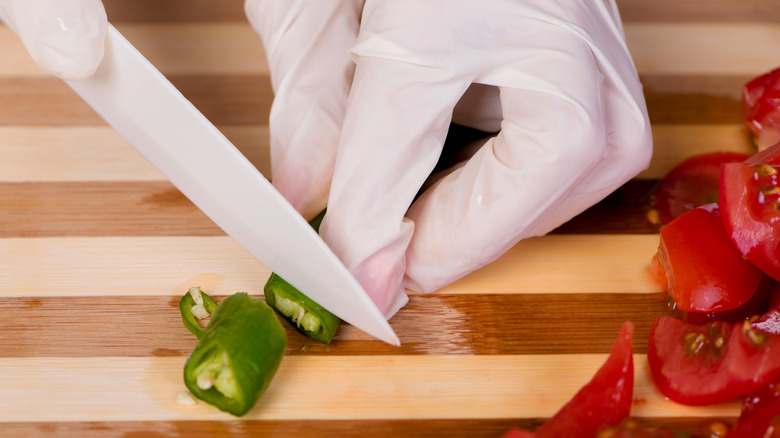 Gloved hands chopping jalapeno peppers