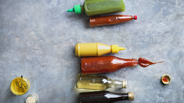 Bottles of ketchup, mustard, relish, and oil are spread out on a table