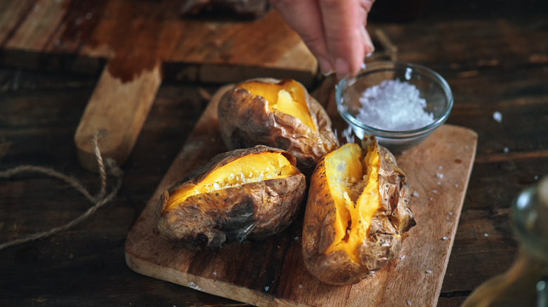 Baked potatoes on chopping board with salt