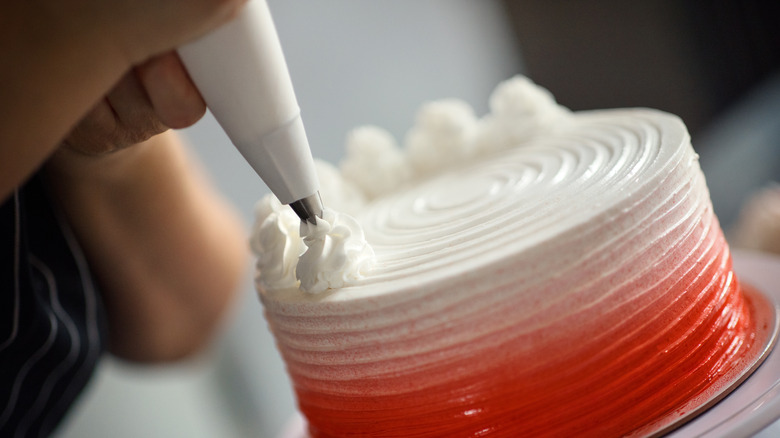 A pastry bag piping frosting onto a cake