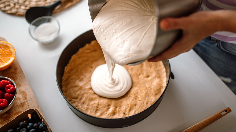 Pouring creamy cheesecake filling into baked crust