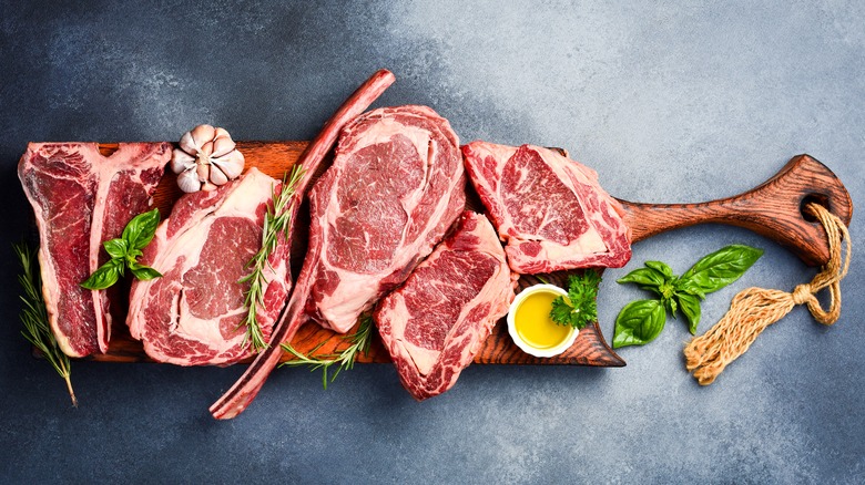 Different cuts of raw steak on a wooden board including ribeye, tomahawk, and T-bone