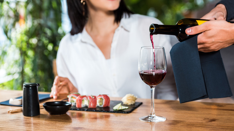 Hands pouring red wine next to sushi platter