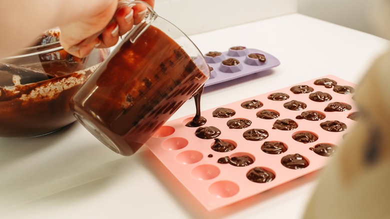 Hand pouring melted chocolate out of glass cup and into pink ice cube mold