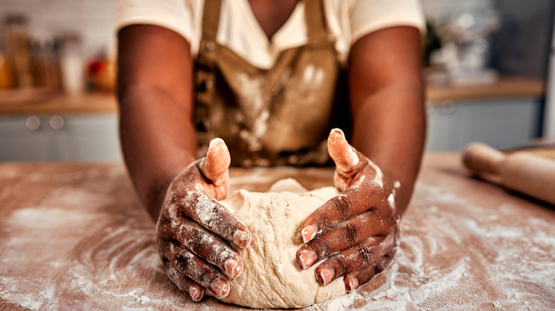 Hands cupping pizza dough on a wooden countertop with flour everywhere