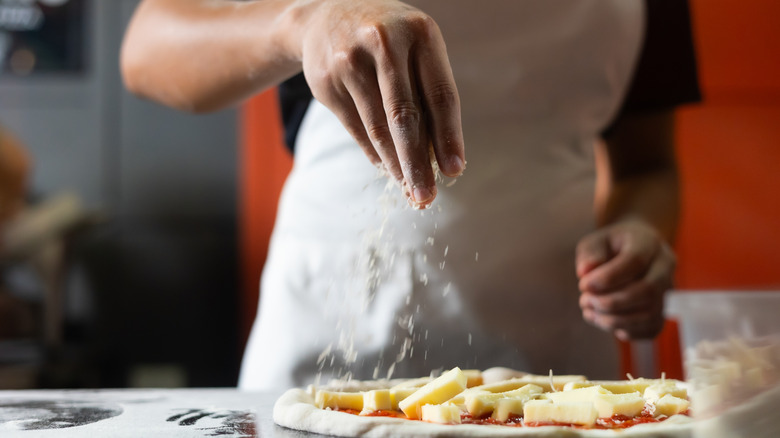 Chef in a white apron topping pizza with cheese