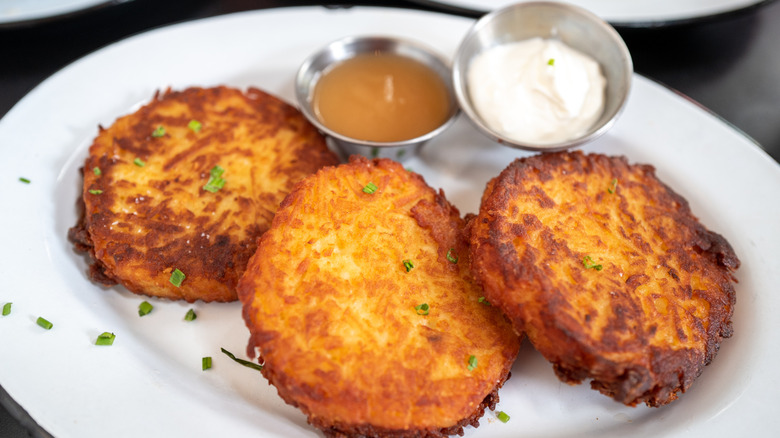 A plate of potato latkes has dipping sauces on the side.