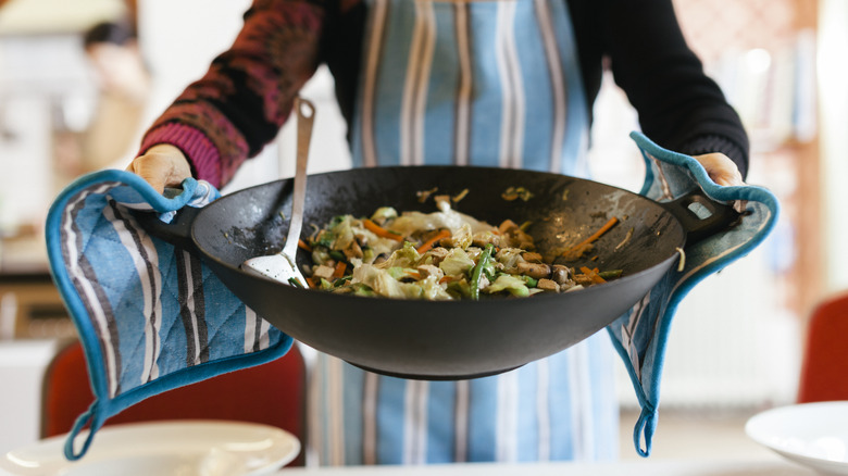 Person holding a large wok full of stir-fried vegetables and tofu