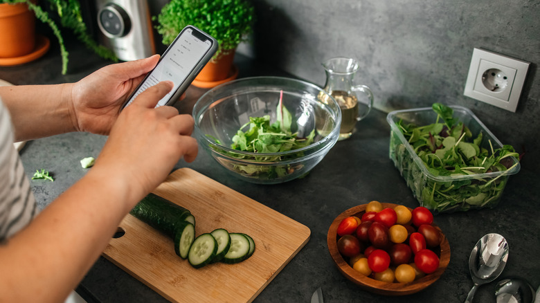 Person chopping vegetables while looking at a recipe on phone