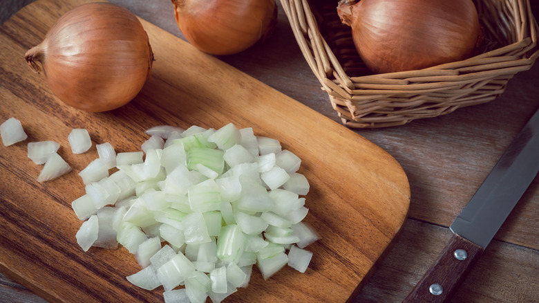 Whole and chopped onions on a wooden cutting board