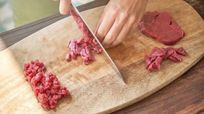 Raw steak being chopped into small cubes on a cutting board