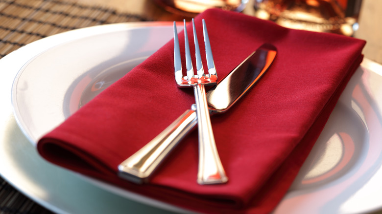 knife and fork on red napkin and white plate