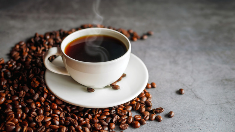 hot cup of coffee surrounded by roaster coffee beans