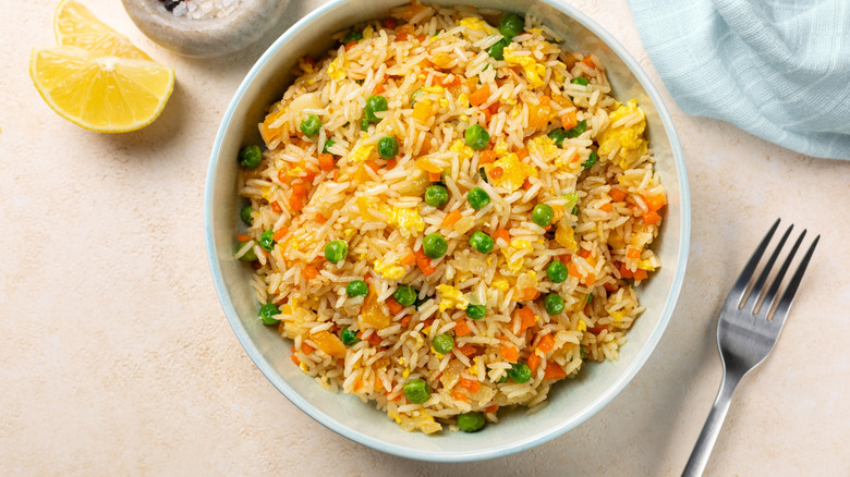 Top view of a bowl with fried rice with egg and vegetables, onion, bell pepper, carrot, green peas.