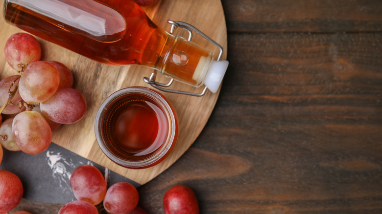 Red wine vinegar in a small glass bowl surrounded by a vinegar bottle and grape bunches