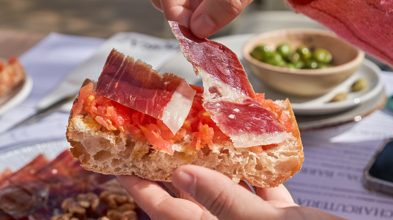 A person placing jamon onto a piece of bread covered in tomato jam