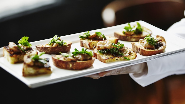 A sever presenting a plate of appetizers with bread, greens, and protein