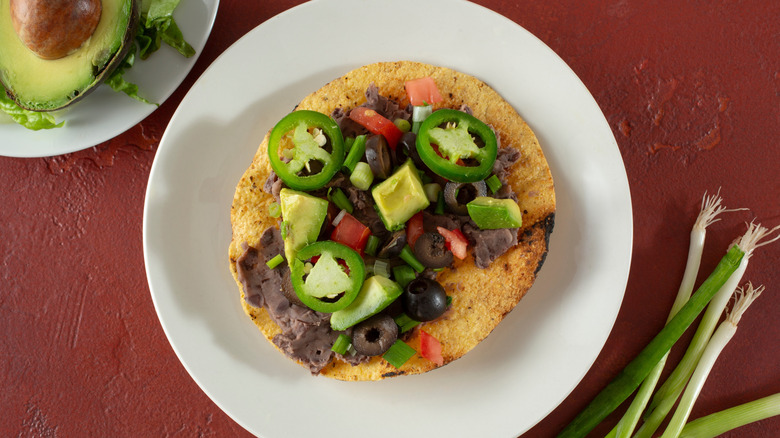 A crispy tortilla is topped with beans, tomatoes, avocado and jalapenos.