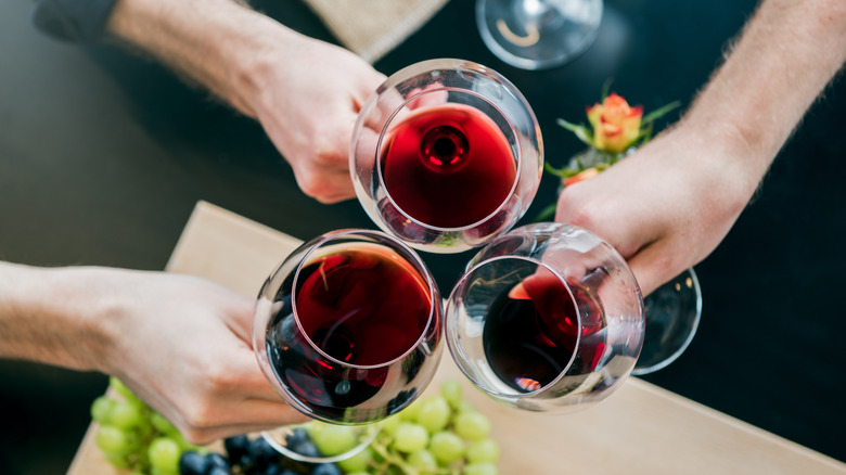 Three hands holding glasses of red wine clink their glasses together in a triangle formation