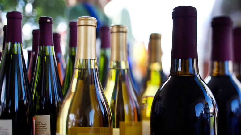 Multiple bottles of sealed red and white wines stand together in a row