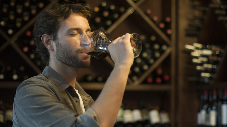 A man standing in a wine cellar takes a small sip of a red wine in a wine glass