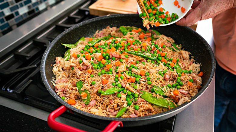 man adding peas and carrots to fried rice