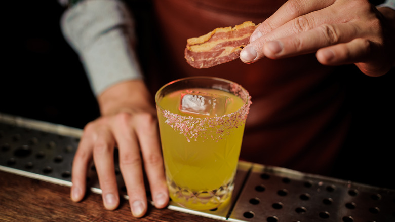 Adding a strip of bacon to an iced cocktail