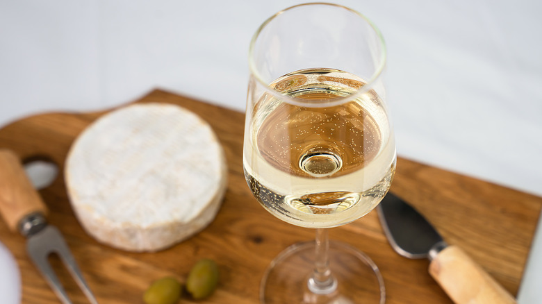 a glass of white wine with brie in the background