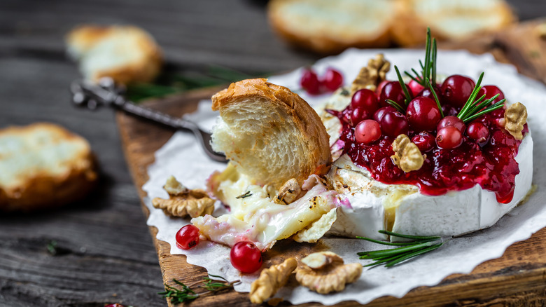 Melted whole Brie topped with cranberry sauce and herbs