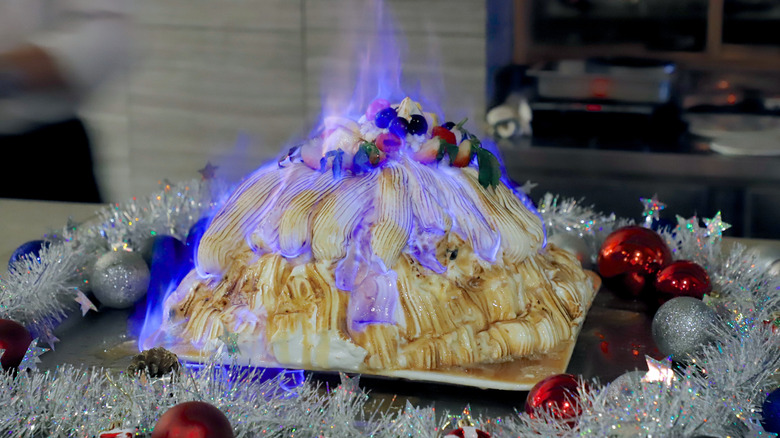 A flaming hot Baked Alaska surrounded by Christmas decorations